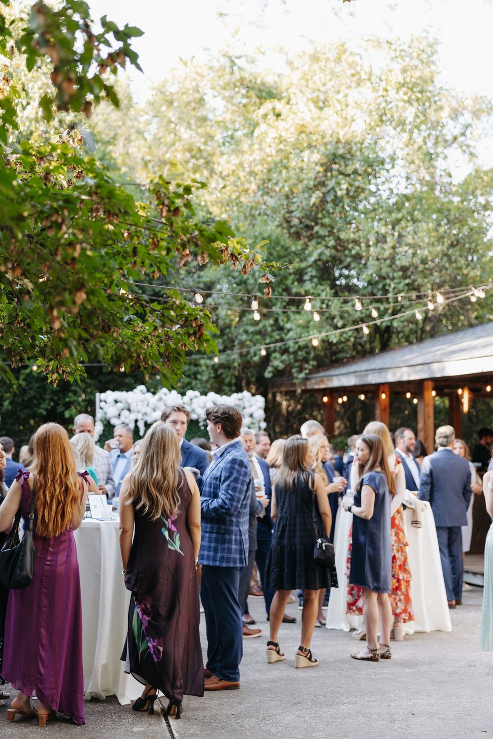 Guests mingle outdoors at an elegant garden wedding reception with string lights and lush greenery.