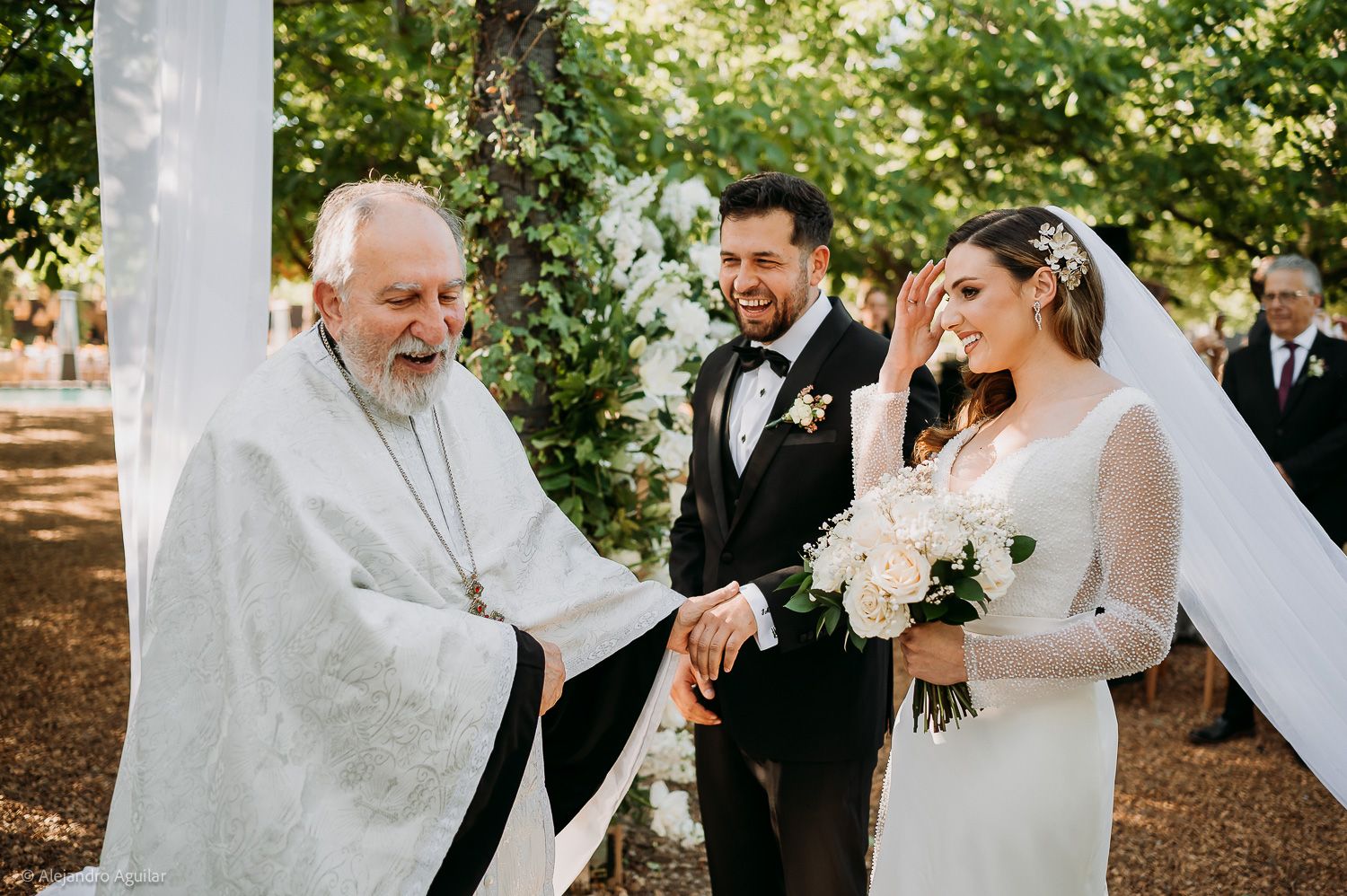 Outdoor wedding ceremony with bride, groom, and officiant exchanging vows under a tree.