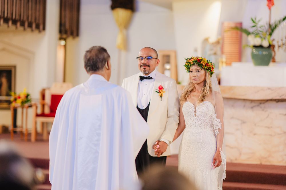 Bride and groom hold hands at church altar during wedding ceremony, officiated by priest, bride wearing floral crown.