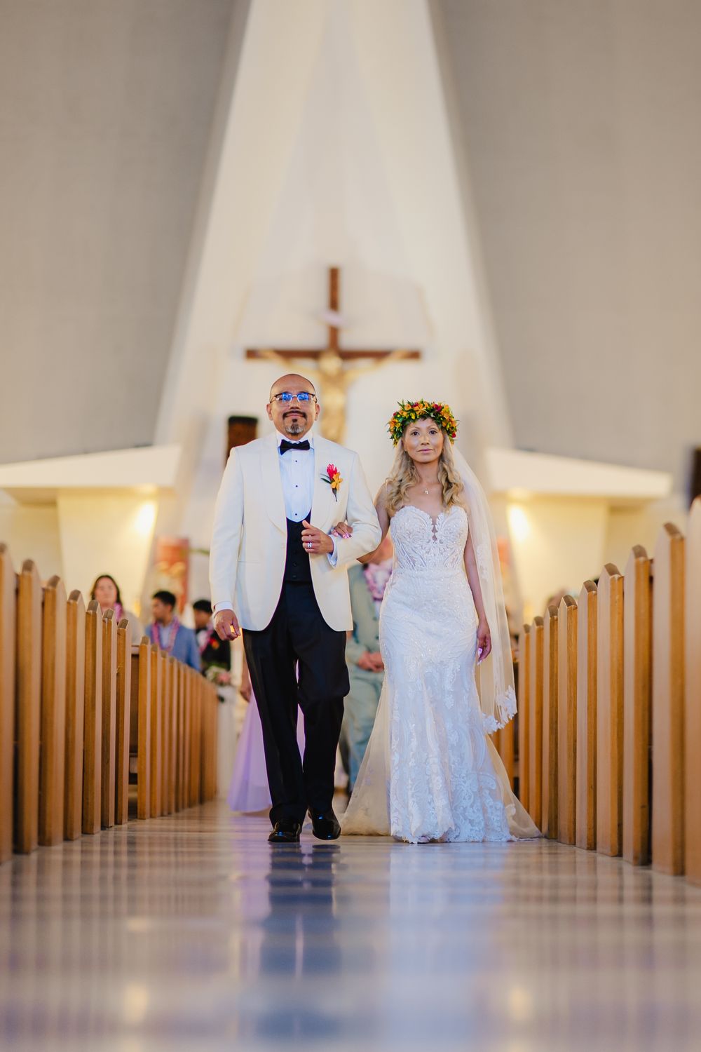 Bride and groom walking down church aisle after wedding ceremony, bride wearing floral crown and lace gown.