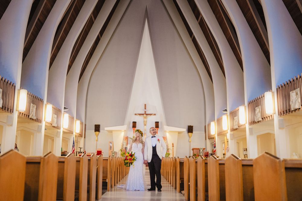 Bride and groom stand together at the altar of a modern Catholic church with wooden pews and a large cross.