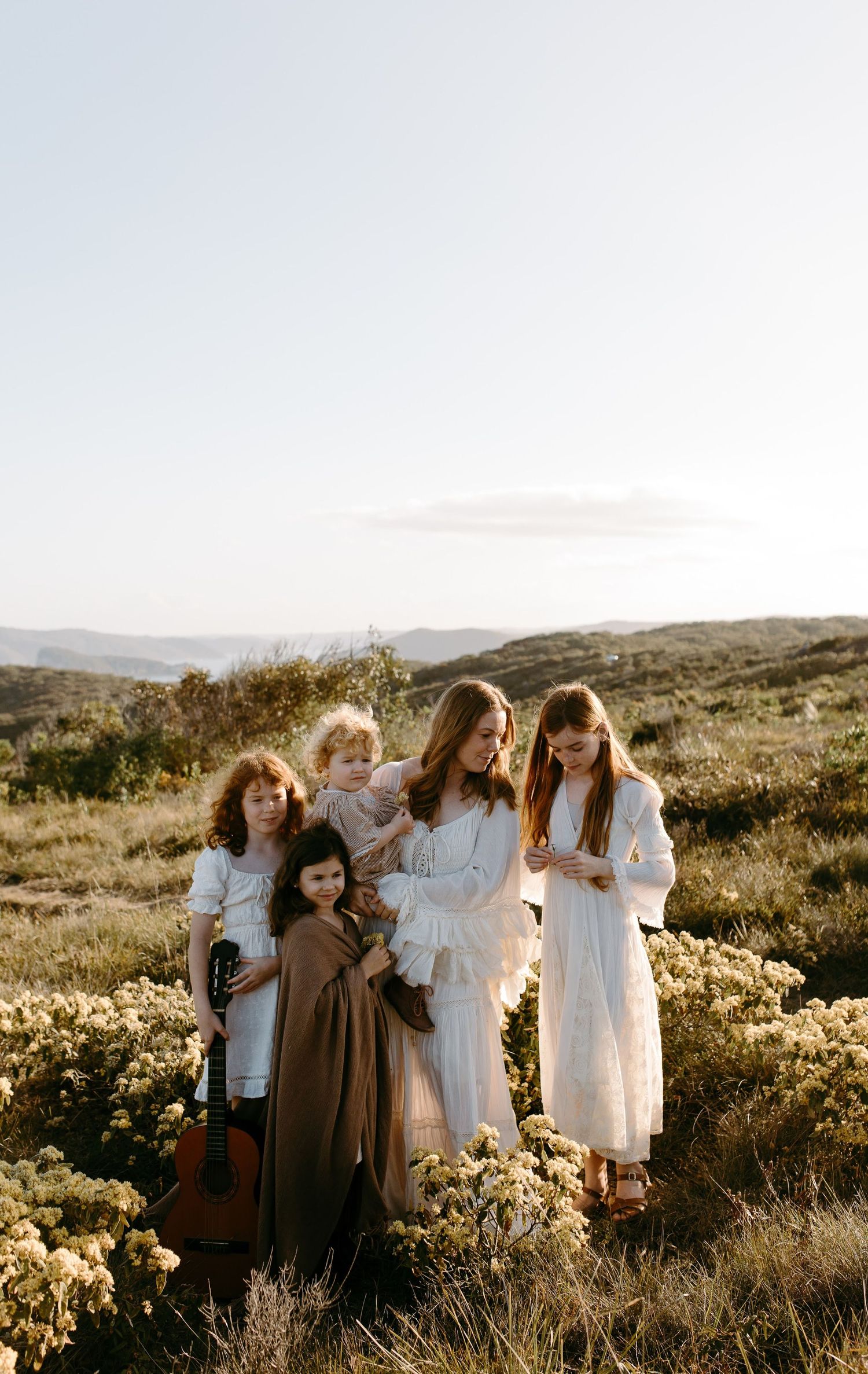 Family walking on a coastal path at golden hour, surrounded by wildflowers with ocean views in the background.