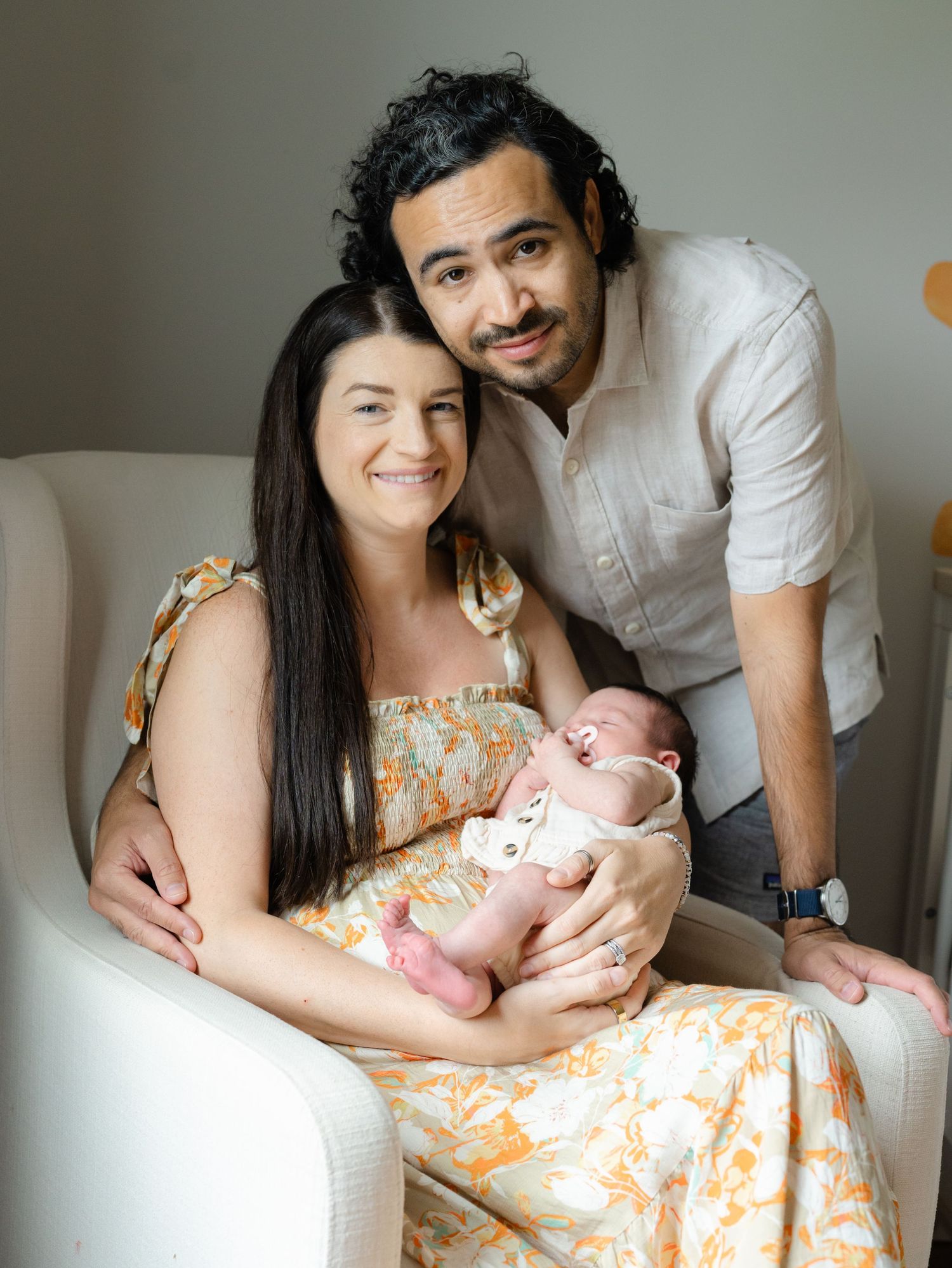 Point pleasant Mother and father hold their newborn girl while sitting in a rocking chair in the nursery.