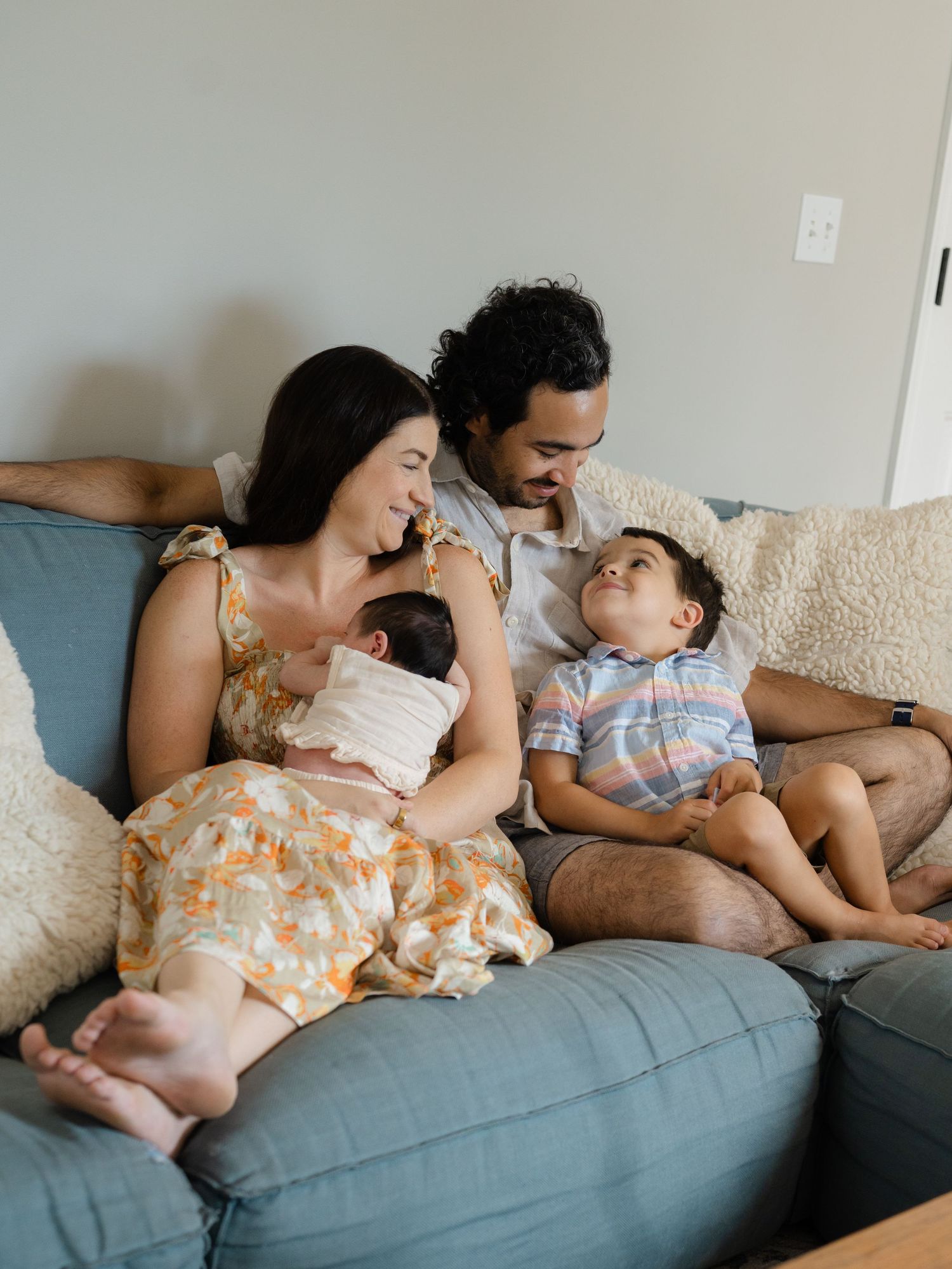 Family of newborn baby snuggle on a blue couch in their home.