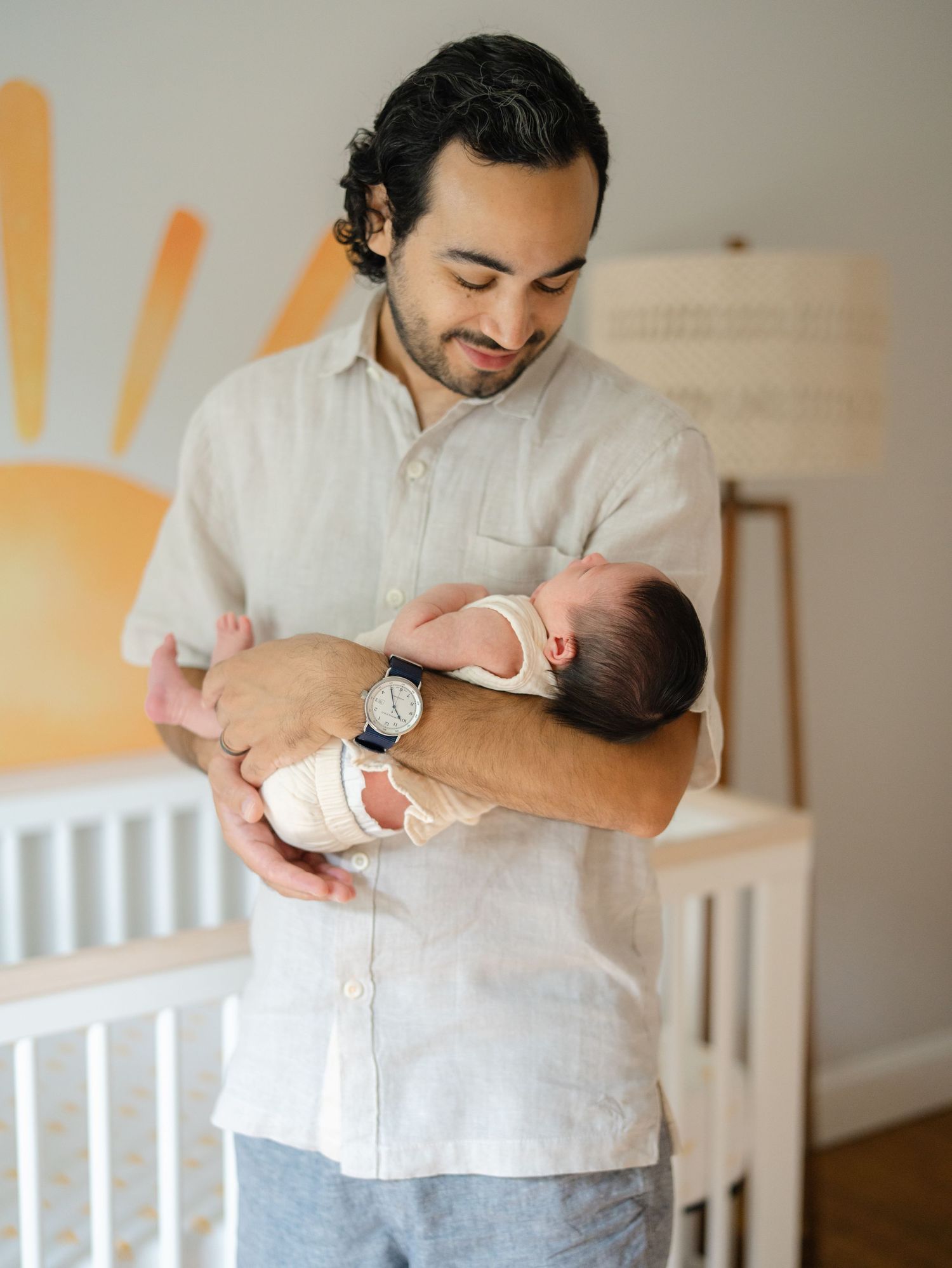 Dad holds newborn baby girl in front of her crib smiling down at her near point pleasant beach.