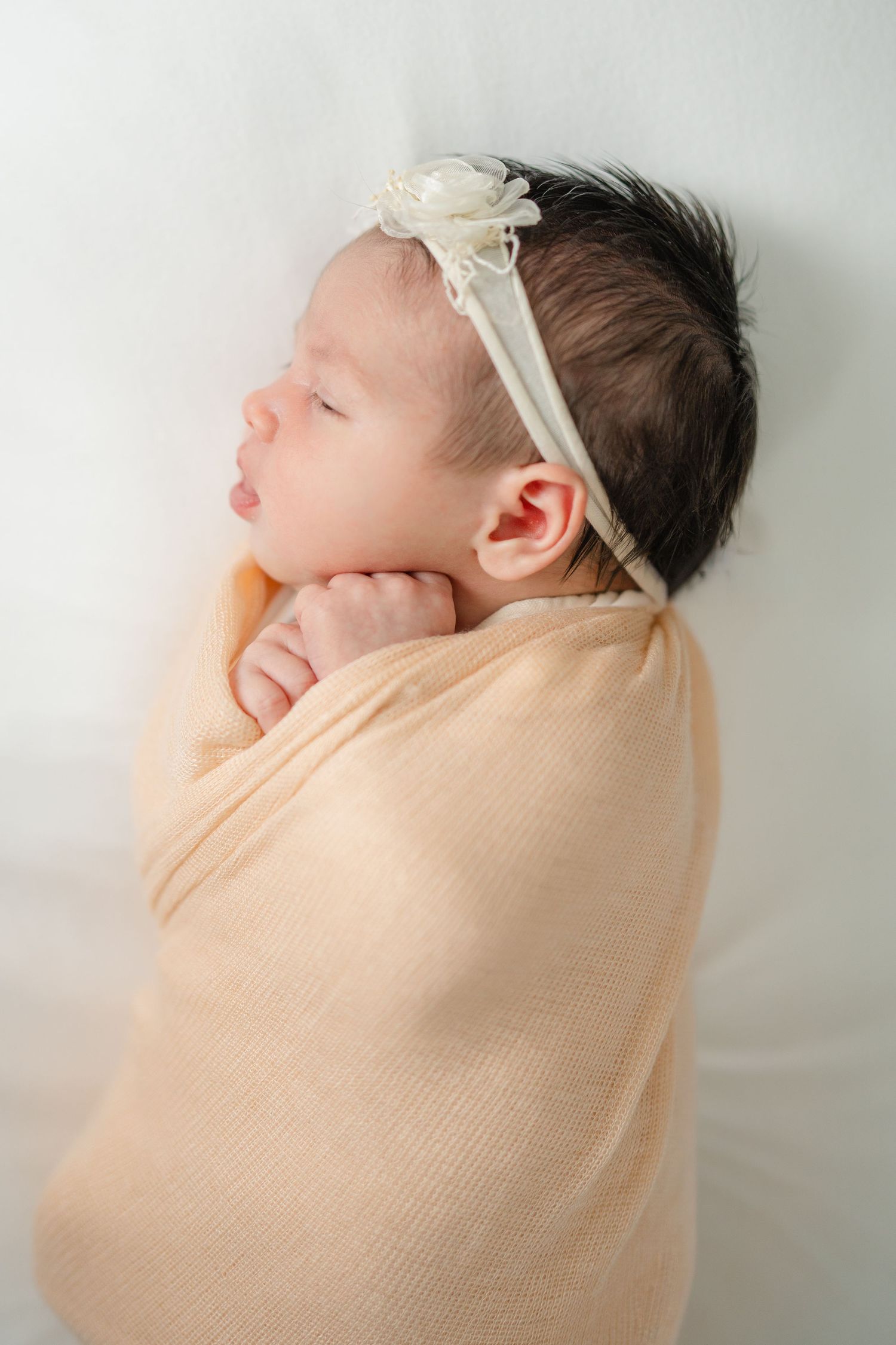 Close up image of baby girl swaddled in a peach colored wrap and white bow.
