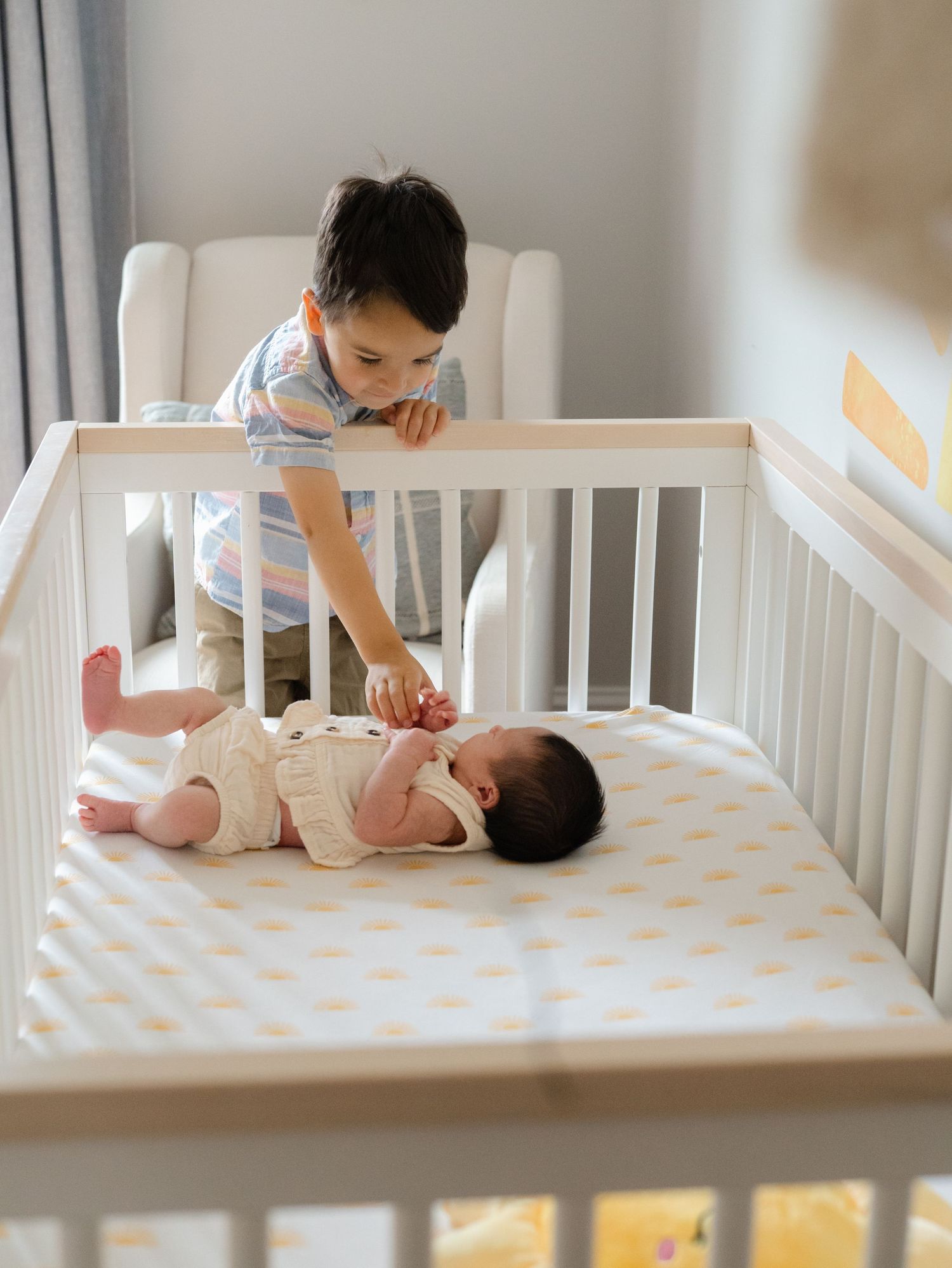 Big boy tickles his sister while she lays in her white crib in brick nj.