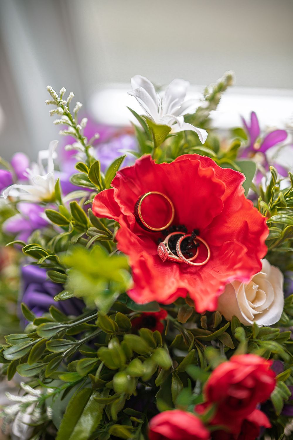 Wedding rings resting inside a vibrant red poppy flower in a colorful bridal bouquet.