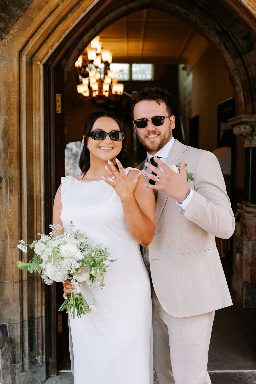 Bride and groom in sunglasses posing at church entrance on wedding day.