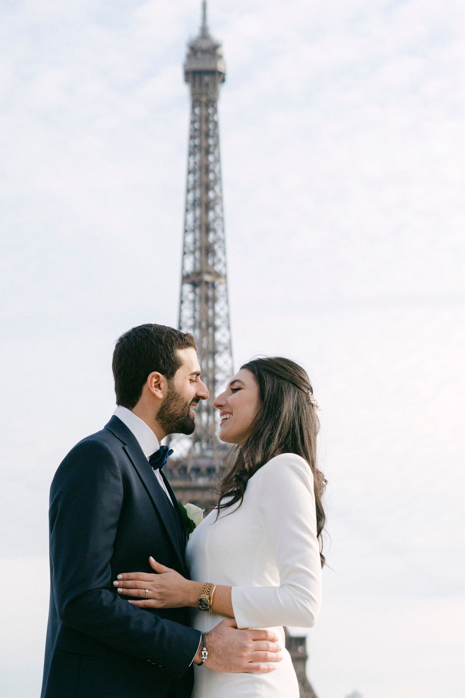Couple sharing a romantic moment in front of the Eiffel Tower in Paris, bride in white dress and groom in navy suit.