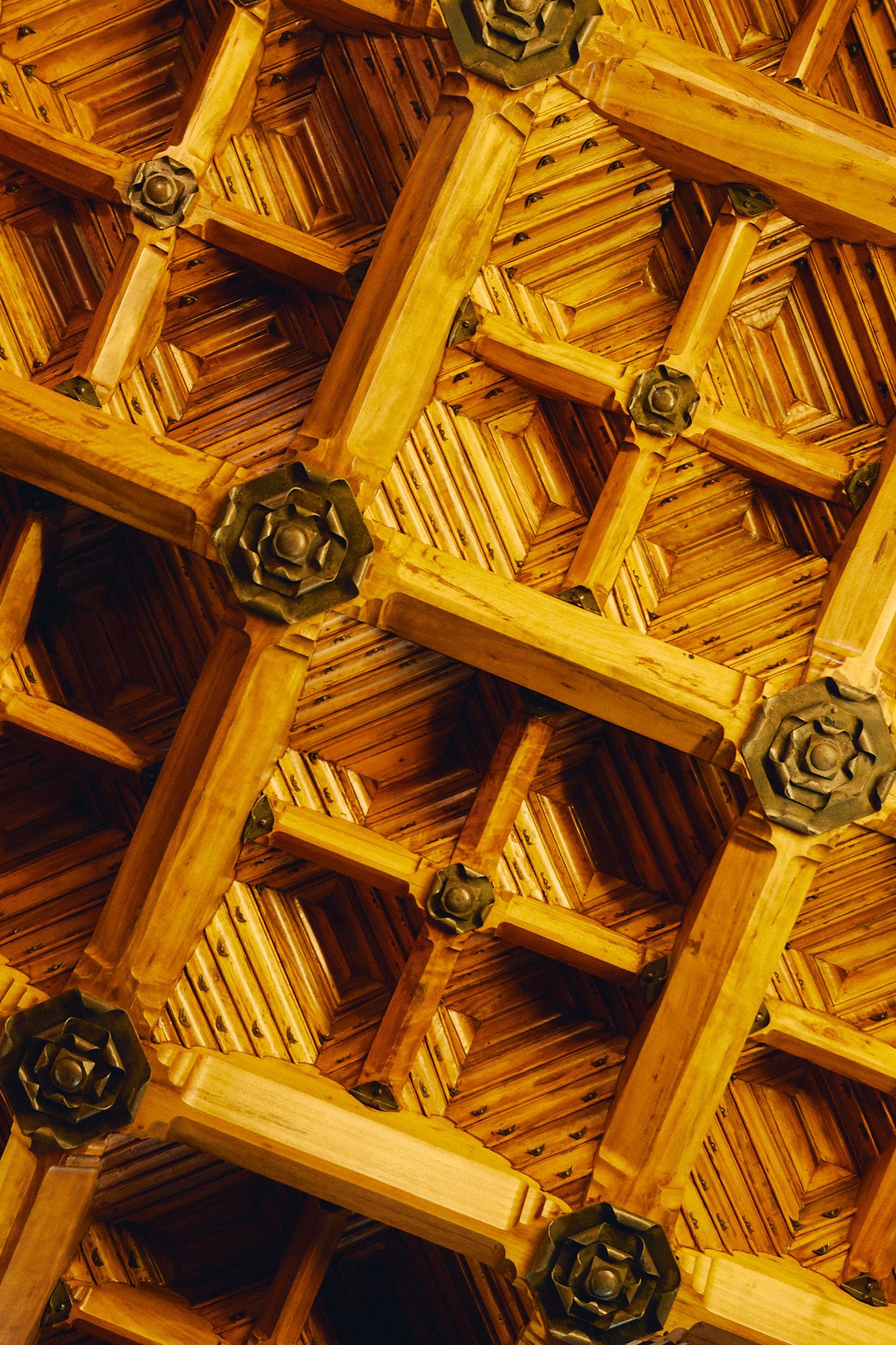 Intricate wooden lattice ceiling with geometric cross patterns and ornate metal rosette accents in warm golden tones.
