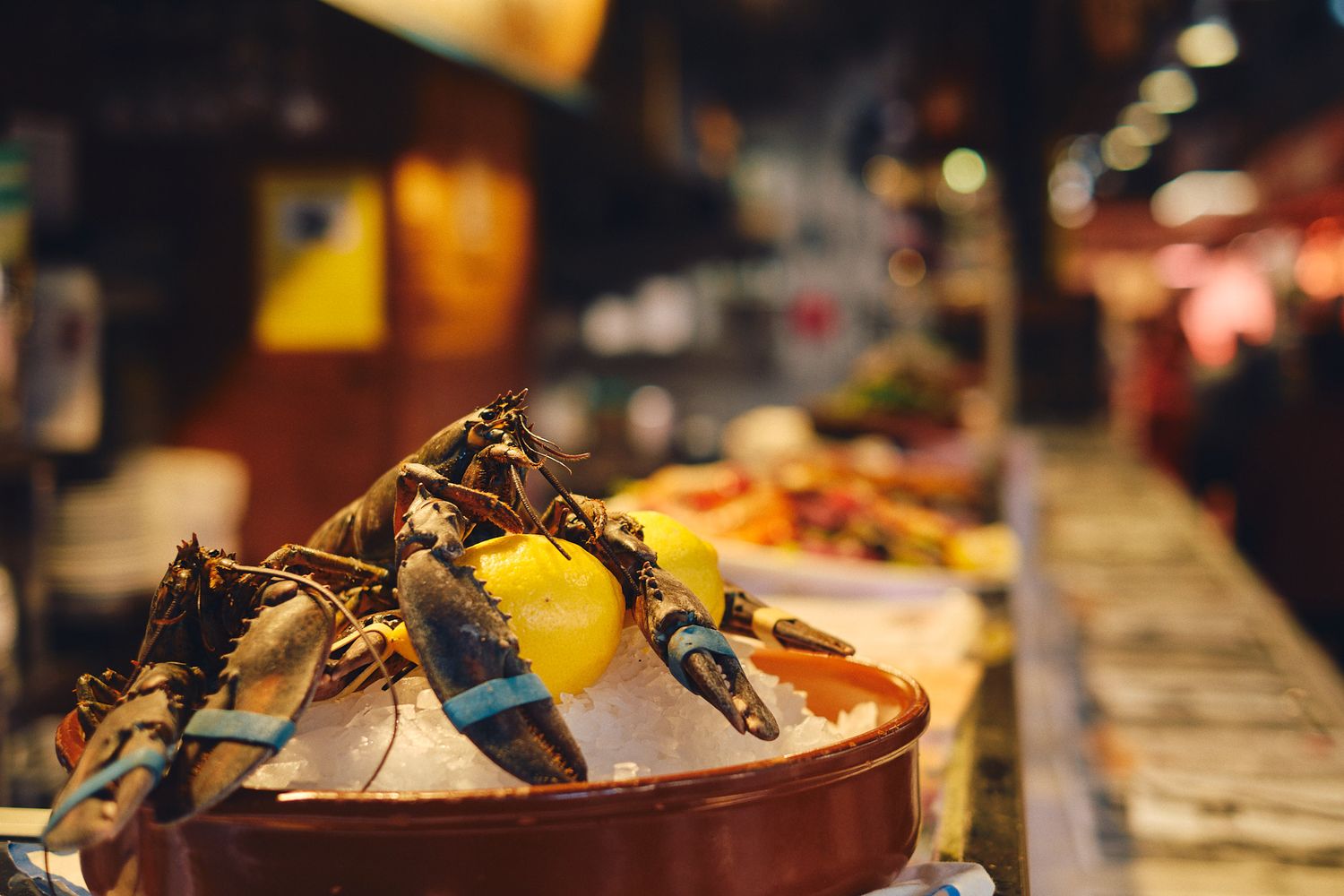 Fresh crabs displayed on ice with lemon in a terracotta bowl at a vibrant seafood market stall.