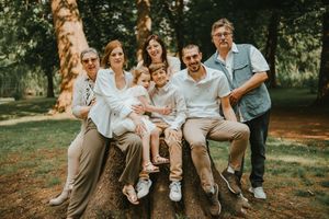 Family of seven posing together on a fallen log in a lush green park during a warm summer day.