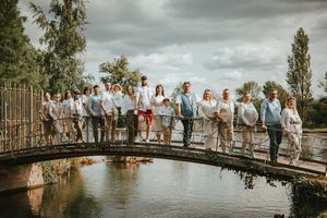 Wedding party posing together on a rustic wooden bridge over a calm pond surrounded by lush greenery.