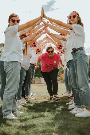 Women in white shirts form a tunnel arch while a bride-to-be in pink runs through during a bachelorette party.
