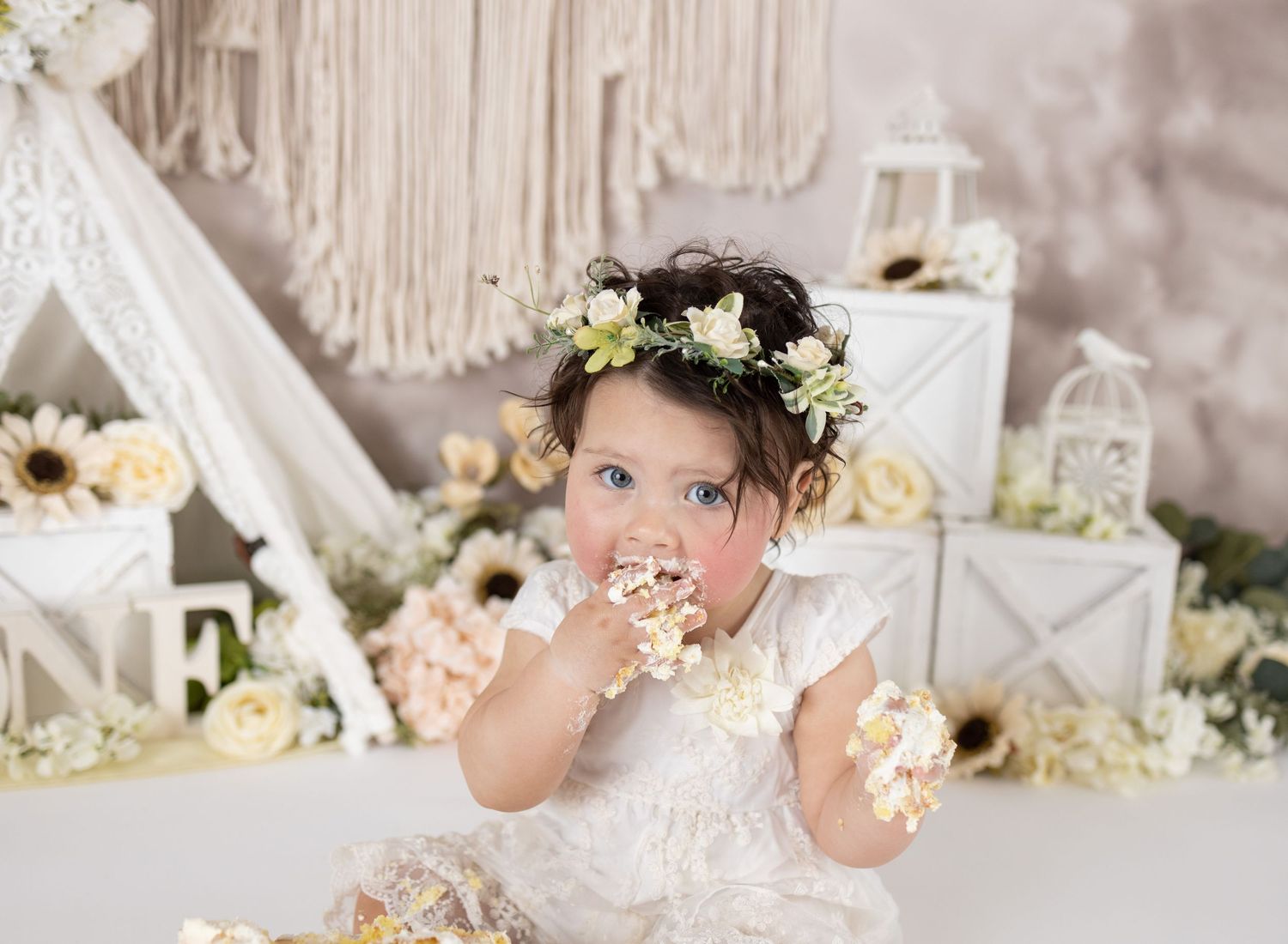 Baby girl in pink dress sits before floral arch with birdcages celebrating her first birthday cake smash.