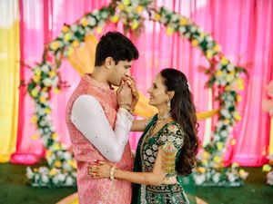 Couple in traditional Indian wedding attire sharing a romantic moment before a floral arch with pink backdrop.