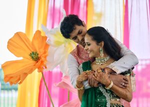Indian couple in traditional attire embracing joyfully at a colorful wedding ceremony with vibrant floral decorations.