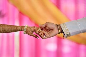 Indian bride and groom holding hands with henna mehndi and gold bangles at a traditional wedding ceremony.