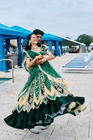 Indian bride in a stunning green lehenga twirling with groom by a poolside at their wedding celebration.
