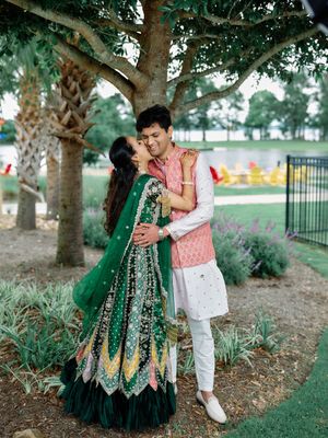 Indian couple sharing a romantic kiss under a tree in a lush garden, dressed in traditional wedding attire.