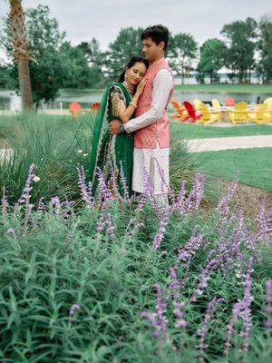 Indian couple in traditional attire embracing among purple wildflowers in a lush garden setting.
