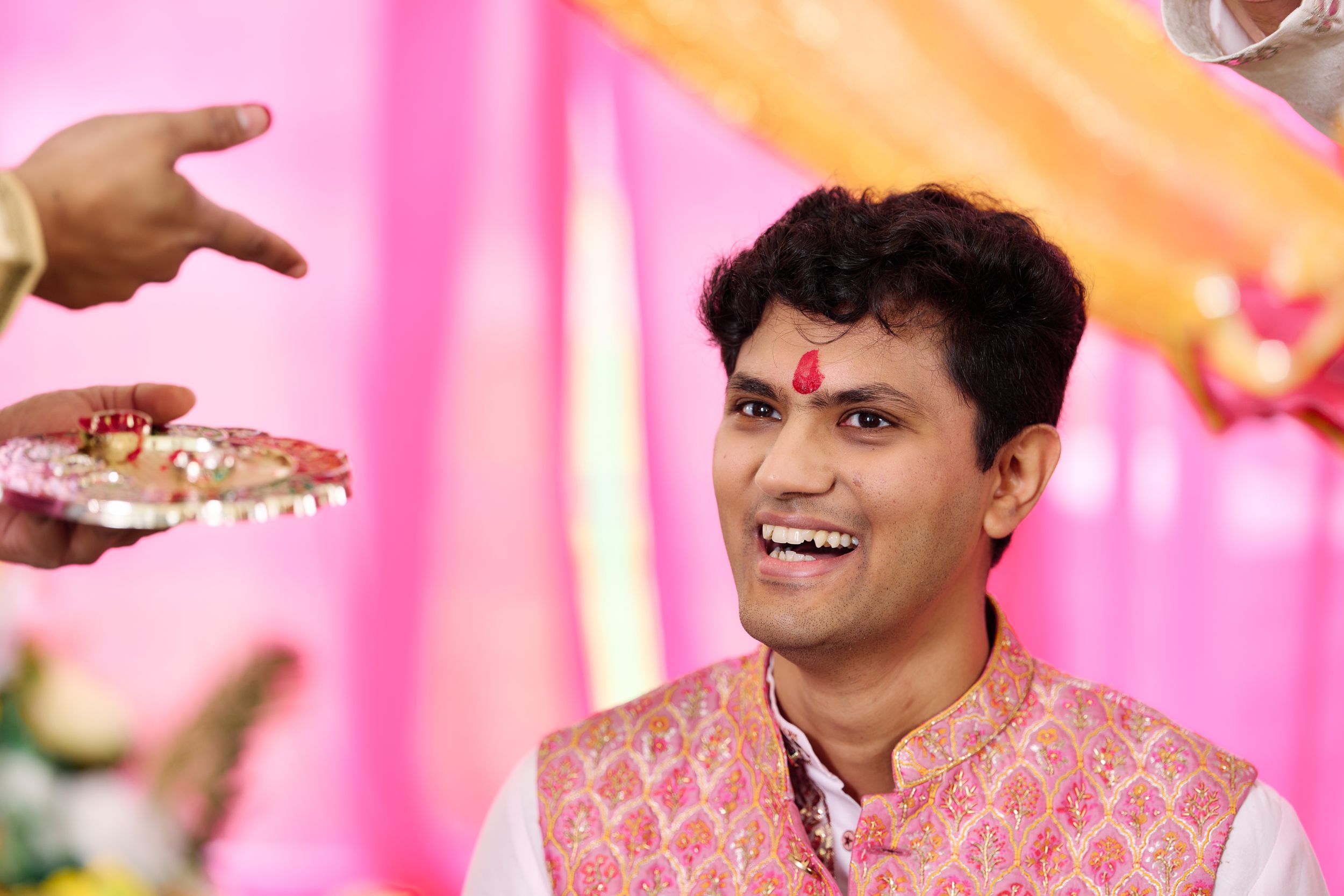 Smiling Indian groom in pink embroidered sherwani during traditional Hindu wedding ceremony with decorative thali.
