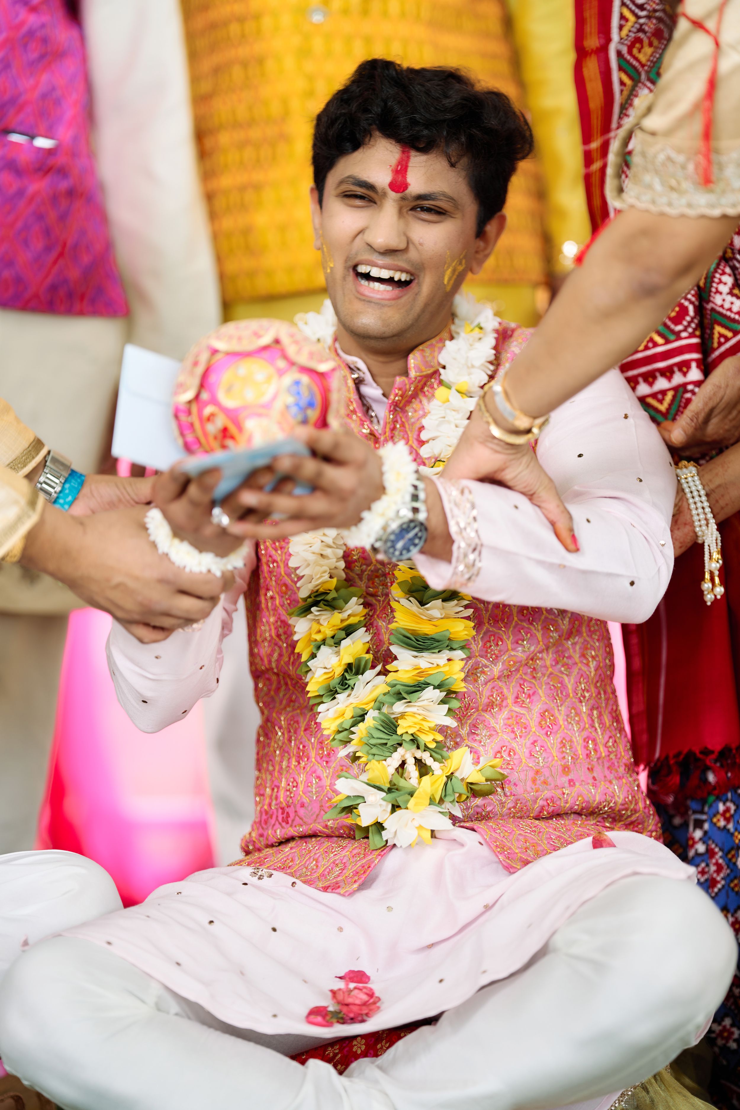 Laughing Indian groom in pink kurta wearing flower garland during traditional wedding ceremony rituals.