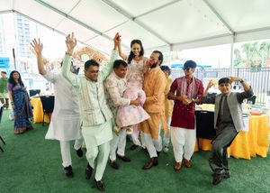 Joyful Indian wedding guests dancing and celebrating under a white tent during a traditional ceremony.