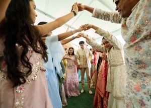 Guests forming a celebratory arch for couple at a vibrant Indian wedding ceremony under a white tent.