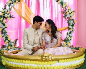 Indian couple in traditional attire sitting on decorated swing during wedding ceremony with floral backdrop.