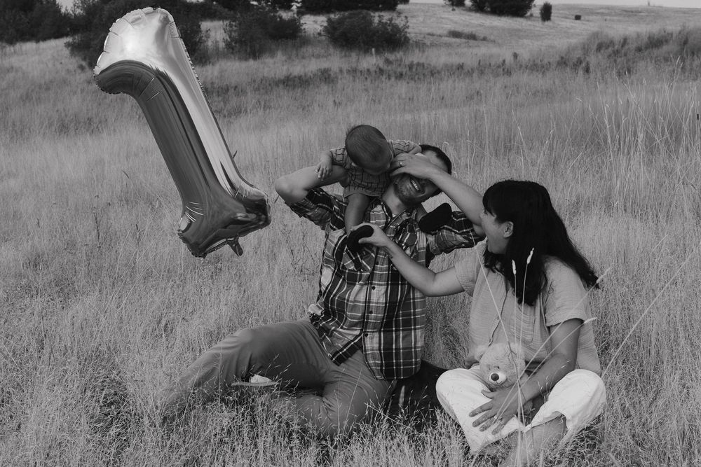 Parents interacting with their one-year-old baby on a picnic blanket in a scenic field in Pullman, Washington.