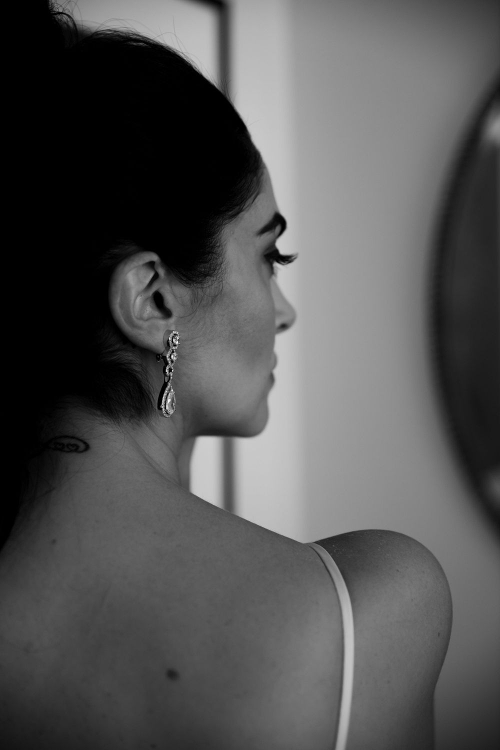 Artistic black and white profile shot highlighting an elegant dangling earring and bare shoulder.