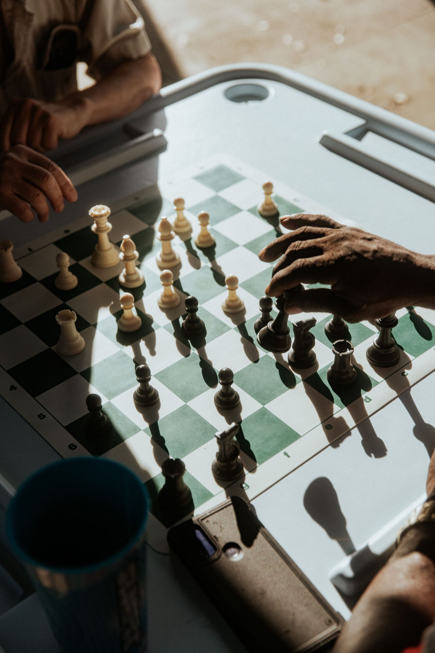 Close-up of a chess game in progress, with a player's hand moving a piece with dramatic lighting, casting deep shadows.