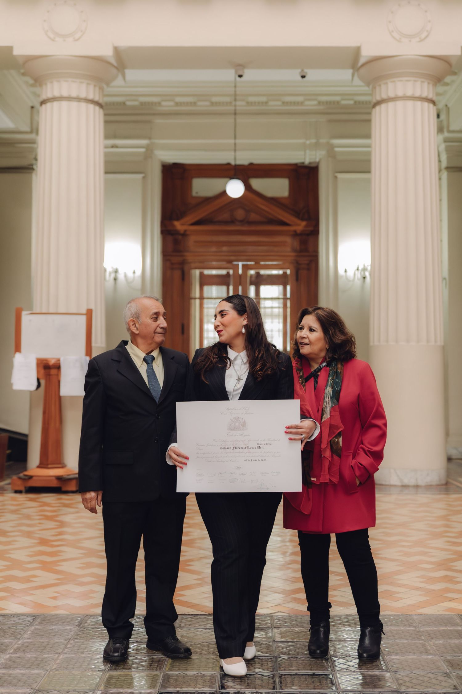 Young graduate and proud parents display diploma certificate in elegant neoclassical building.