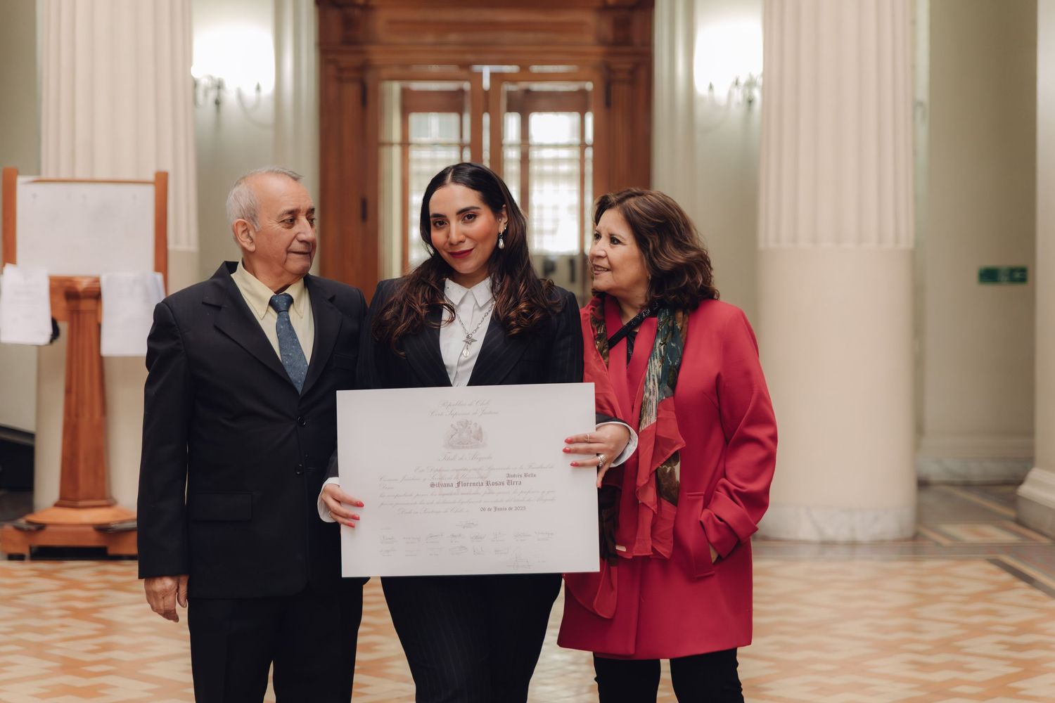Graduate holds diploma flanked by proud family members in a formal building.