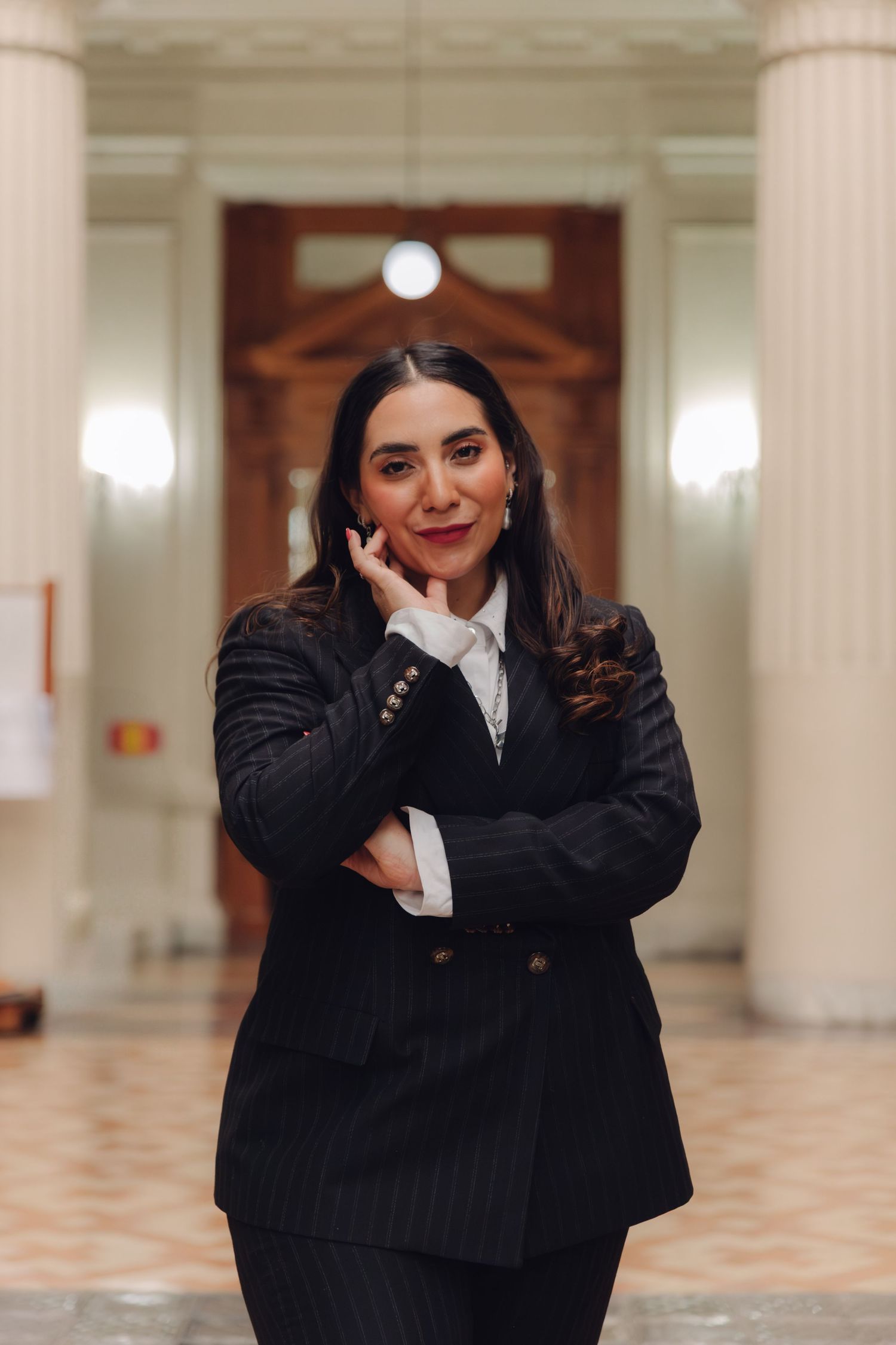 Professional woman in pinstripe suit poses confidently in elegant columned hall.
