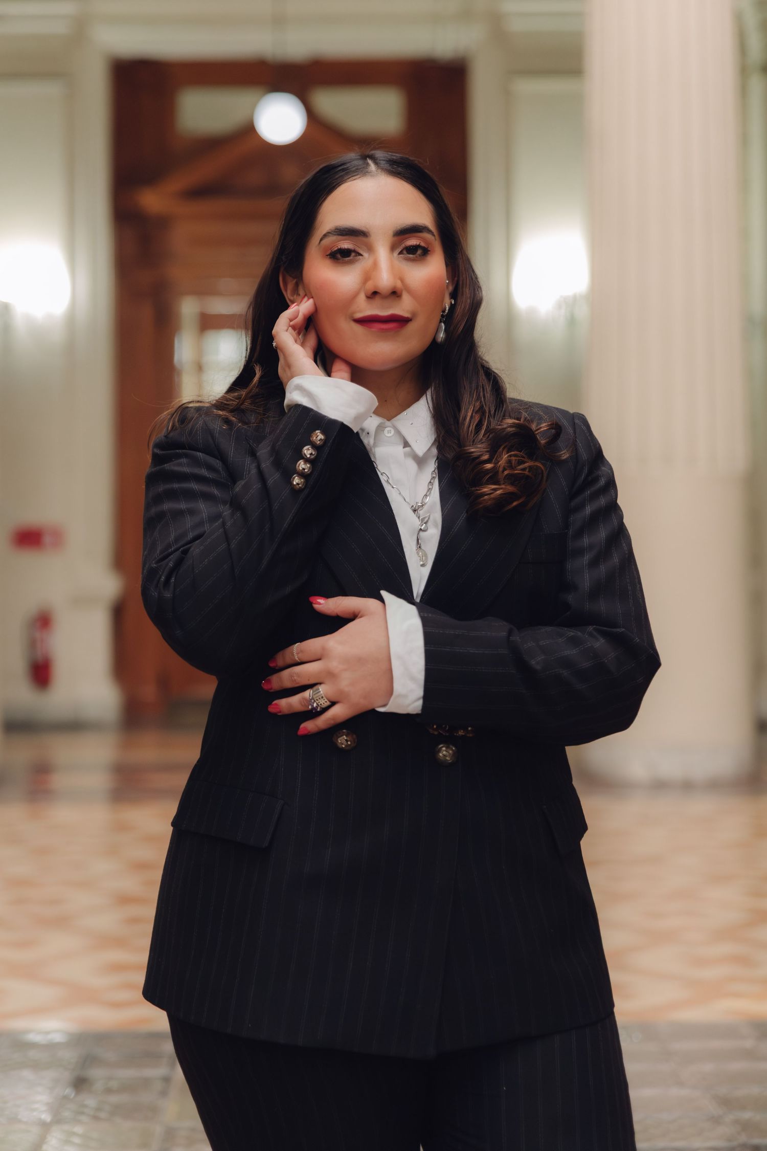 Confident woman in black pinstripe blazer poses in grand architectural interior.