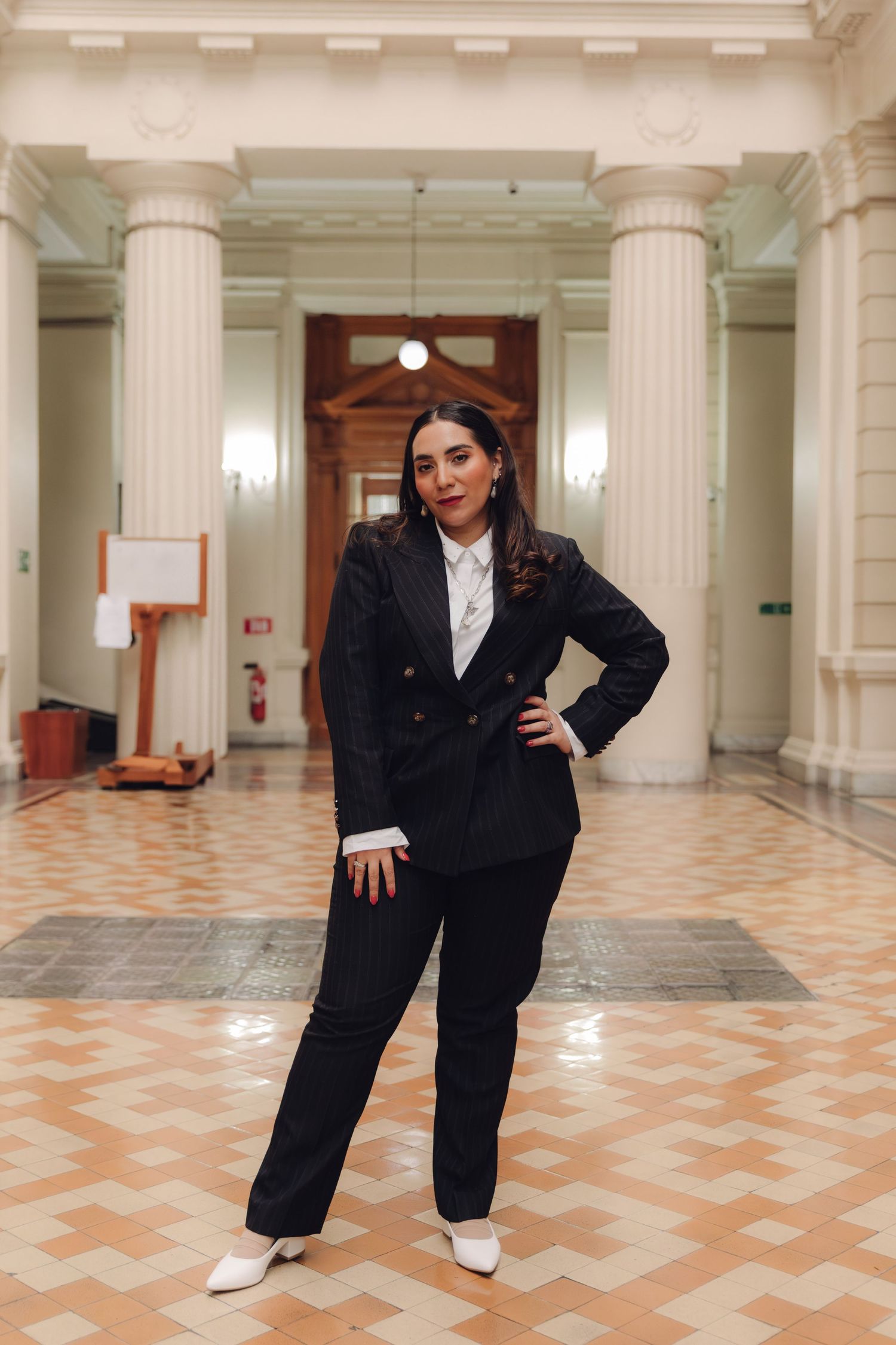 Professional woman in black suit stands confidently in ornate tiled hallway.