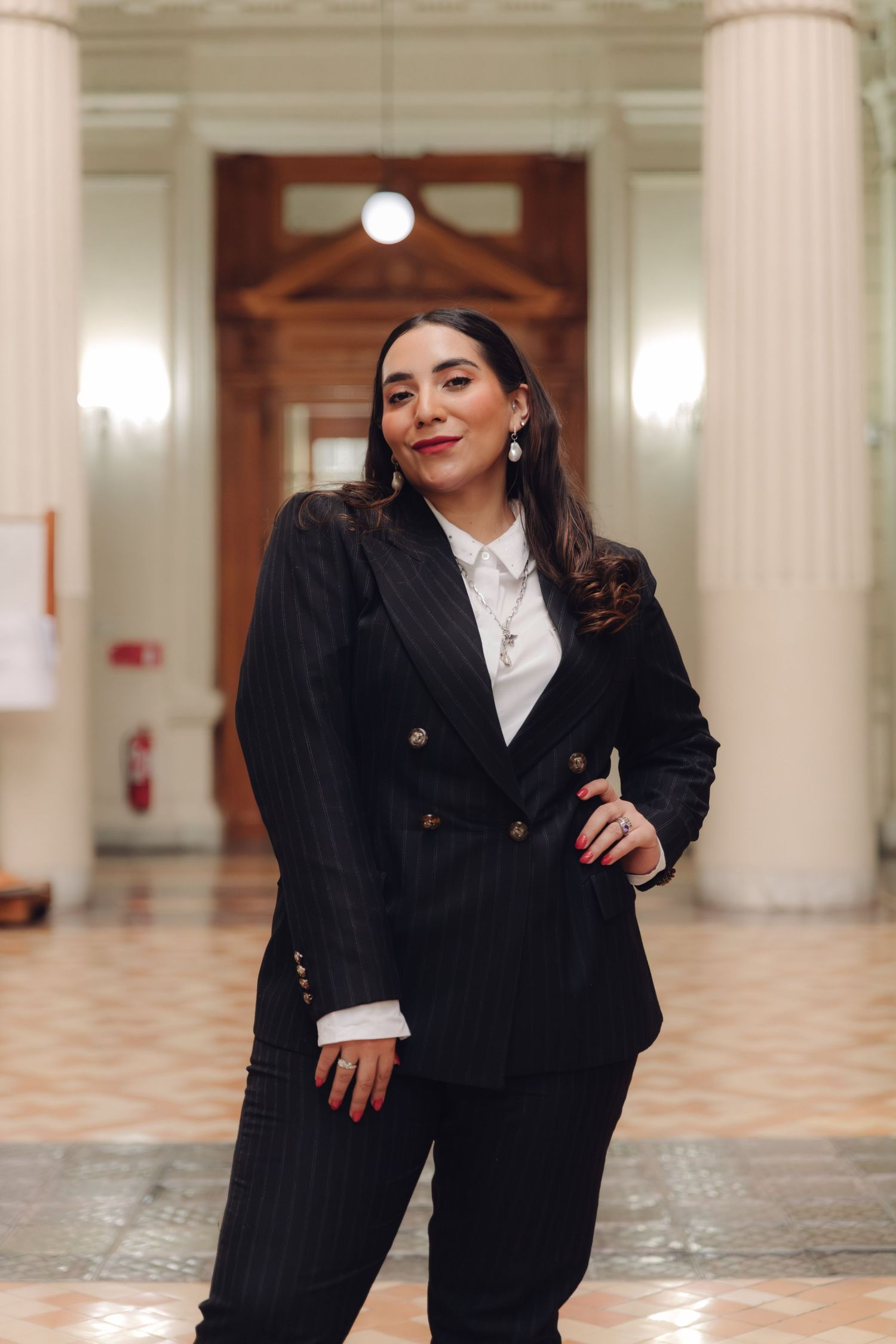 Elegant woman in pinstripe suit poses gracefully in classical columned interior.