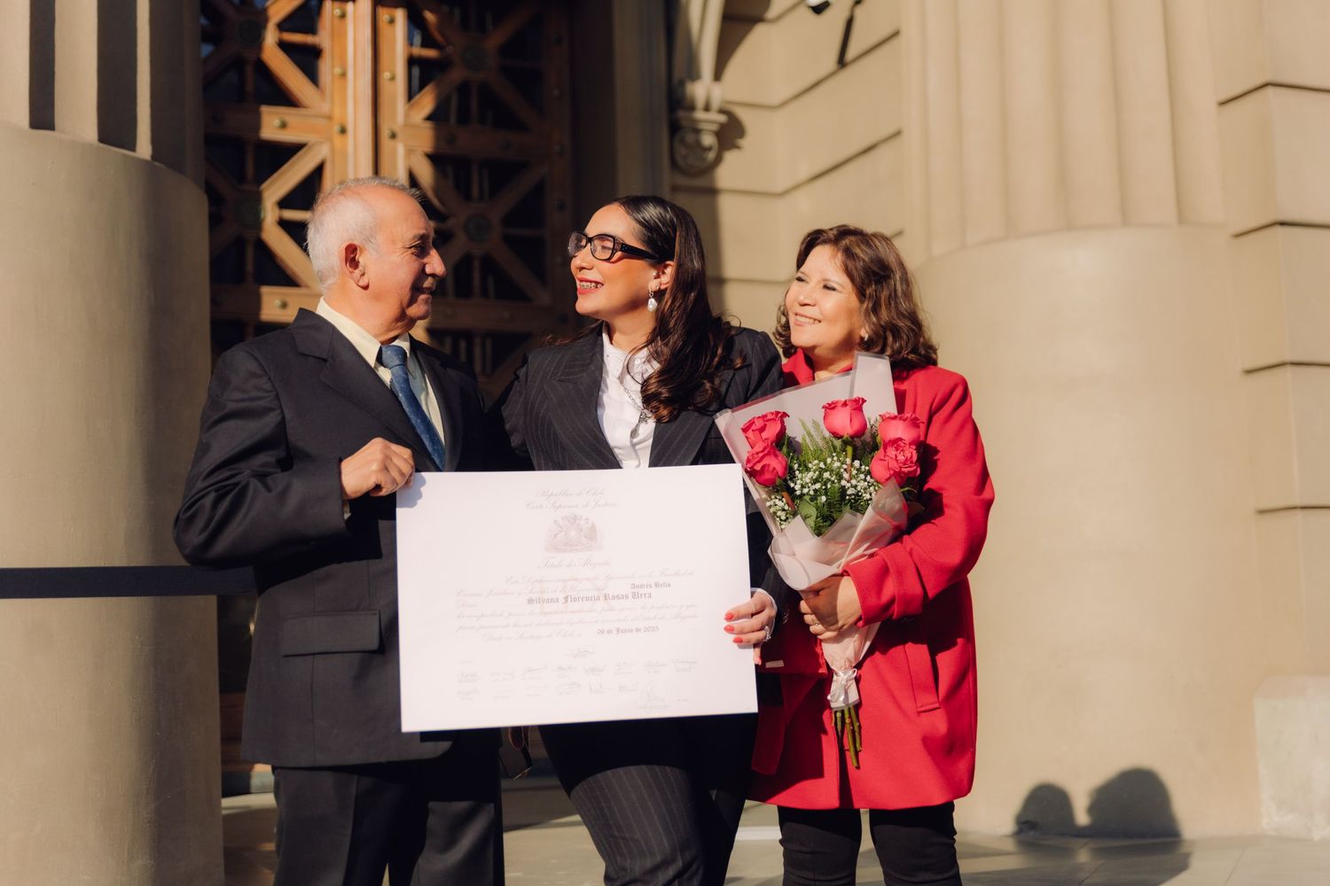 Two older adults and a young woman display a large certificate on building steps.