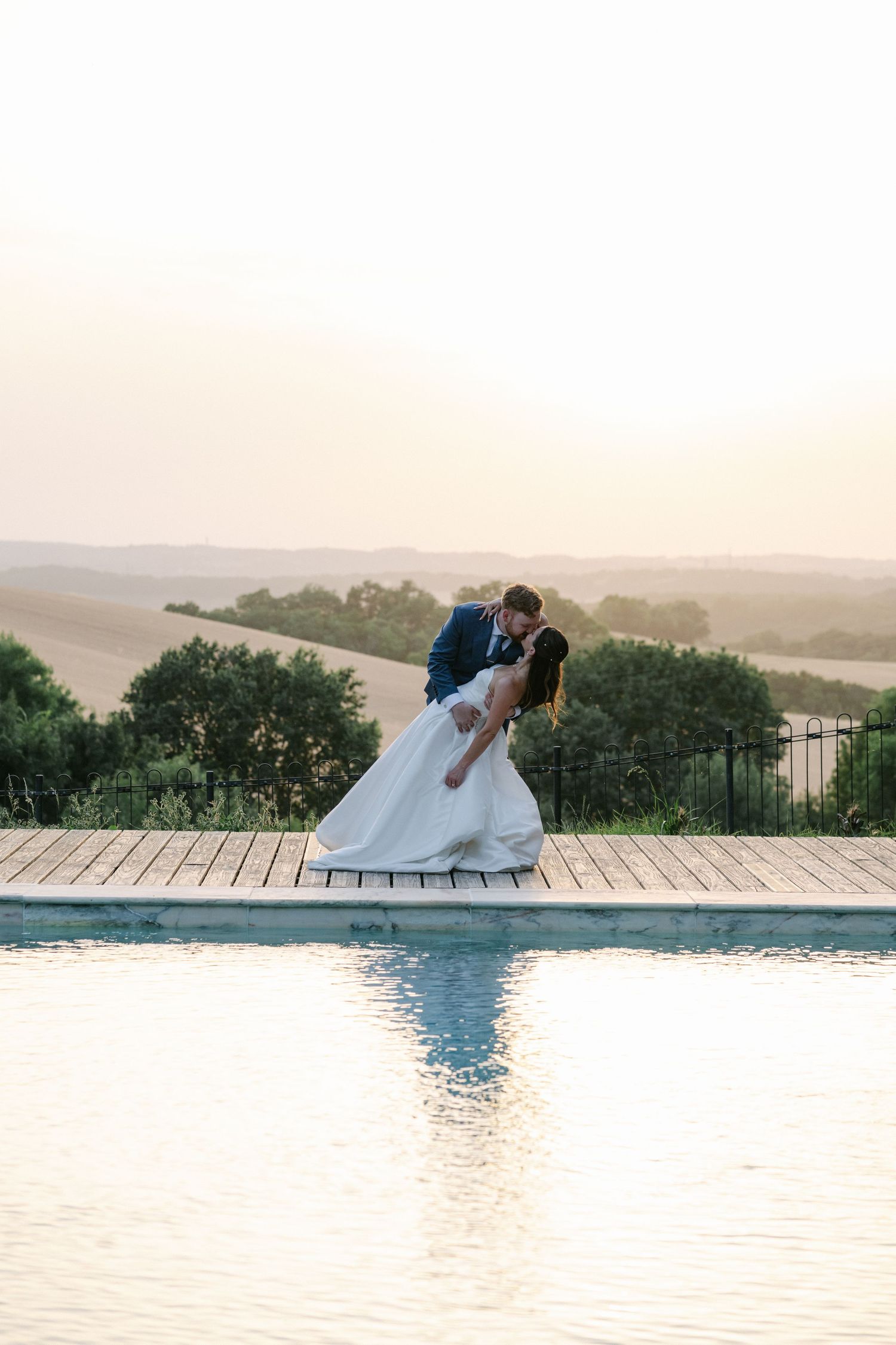 A joyful bride in white gown and groom in blue suit hold hands laughing at sunset during their wedding celebration.
