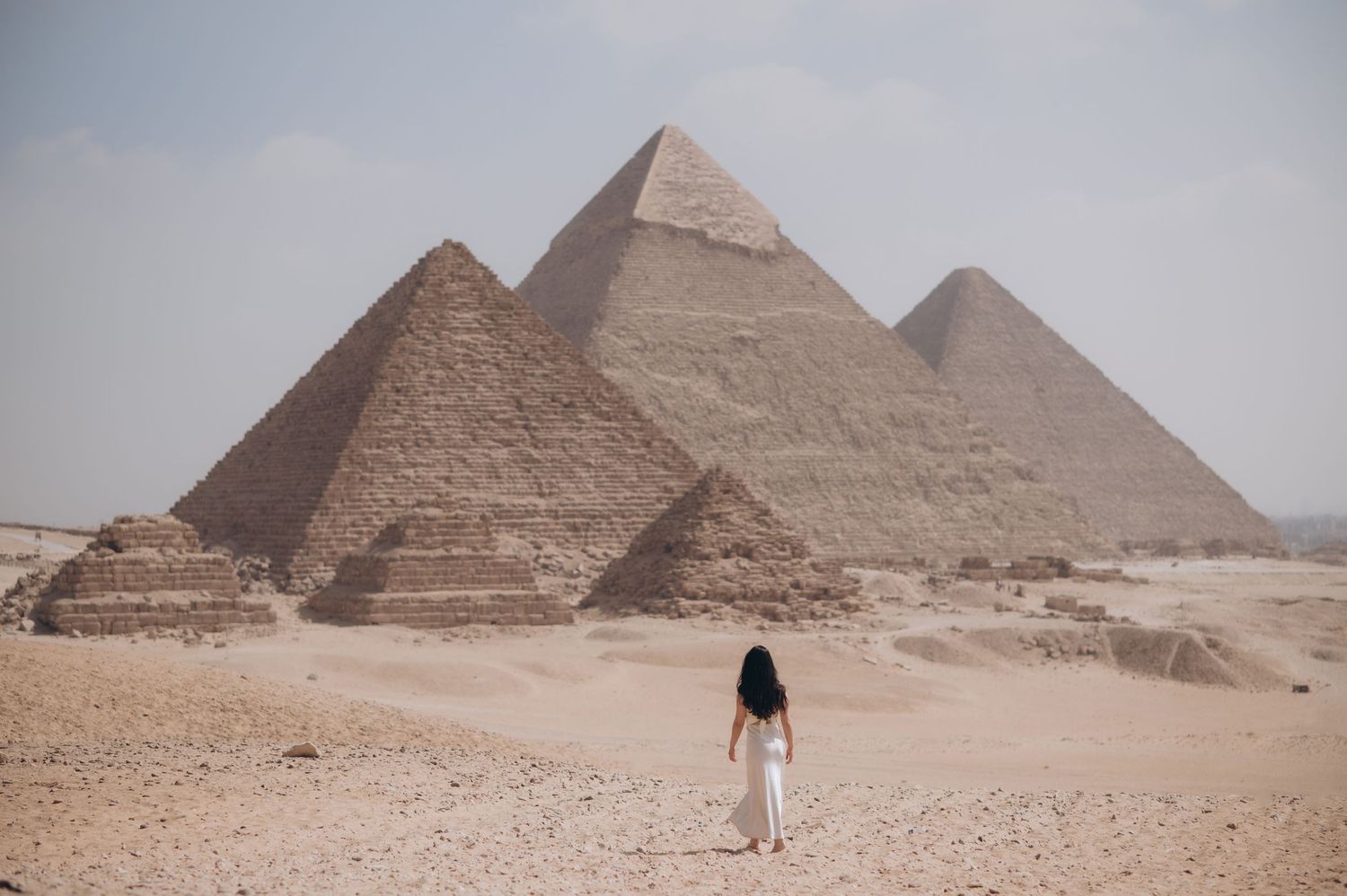 Several views of the ancient Egyptian pyramids in Giza with tourists exploring the desert landscape in the foreground.