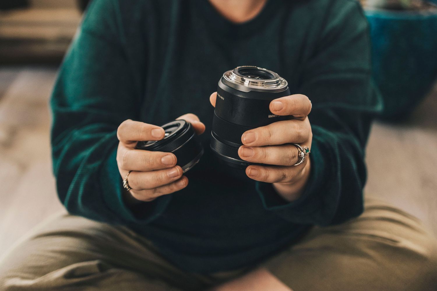 Close-up of hands holding detached camera lens indoors.
