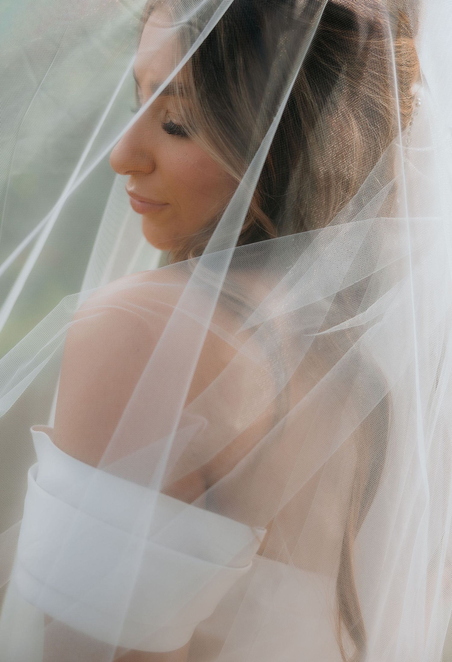 Ethereal bridal portrait with soft white veil creating a dreamy, romantic atmosphere in natural light.