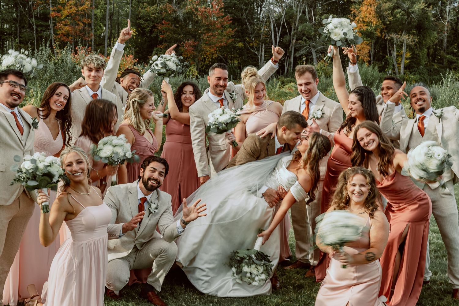 Wedding party celebrates outdoors with joyful expressions while wearing coral and white attire.