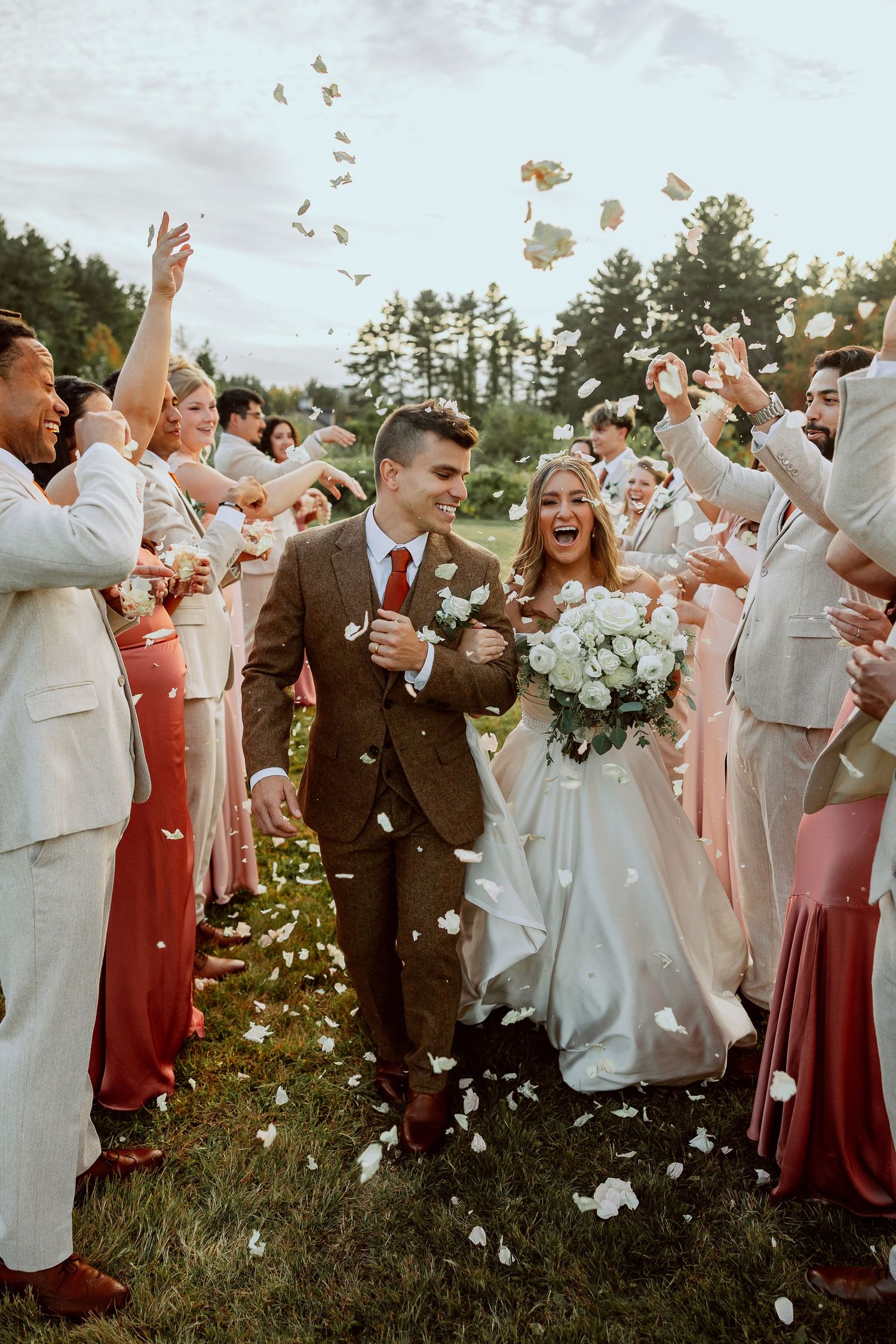 Wedding celebration with confetti being tossed in the air as newlyweds walk through crowd in outdoor garden setting.