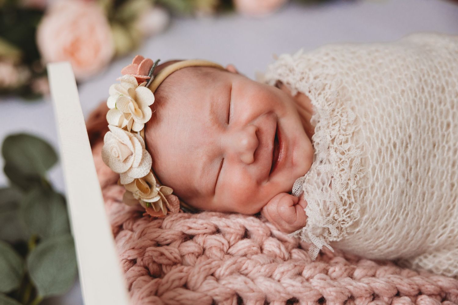 Newborn baby sleeping peacefully in white wicker basket with fluffy fur lining outdoors.