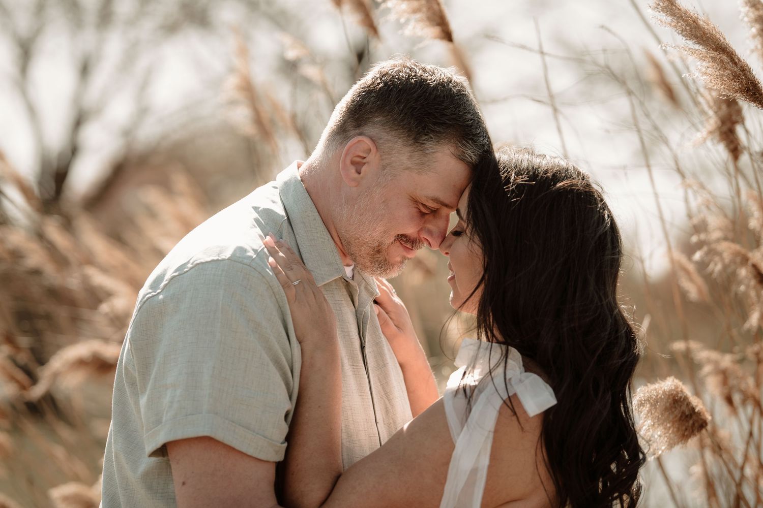 A romantic outdoor portrait shoot in warm sunlight with pampas grass framing the couple's intimate moment.