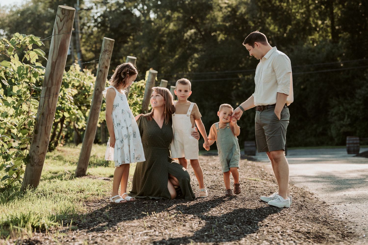 Family enjoying a warm summer evening together outdoors by rustic wooden posts in golden sunlight.